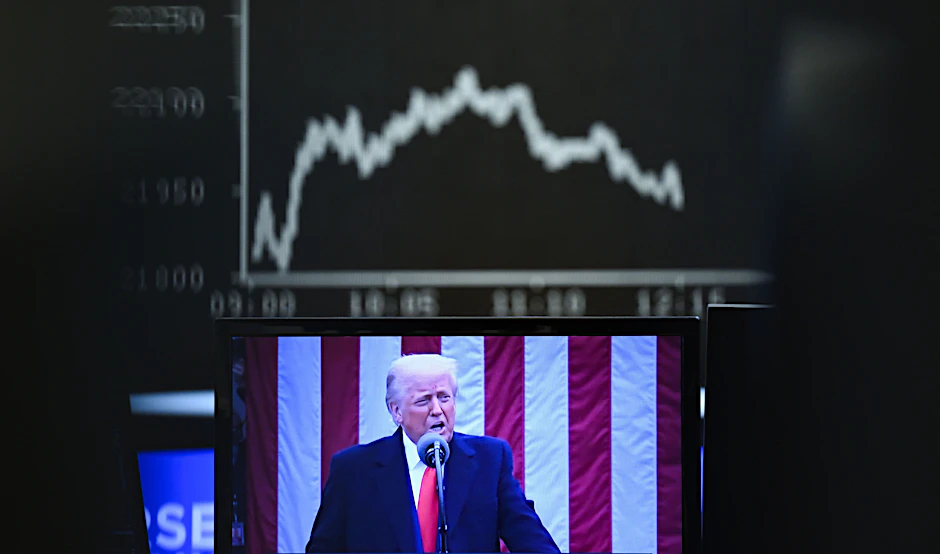 Auf einem Monitor, vor dem US-Präsident Donald Trump zu sehen ist, zeigt die Anzeigetafel mit der Dax-Kurve fallende Kurse.