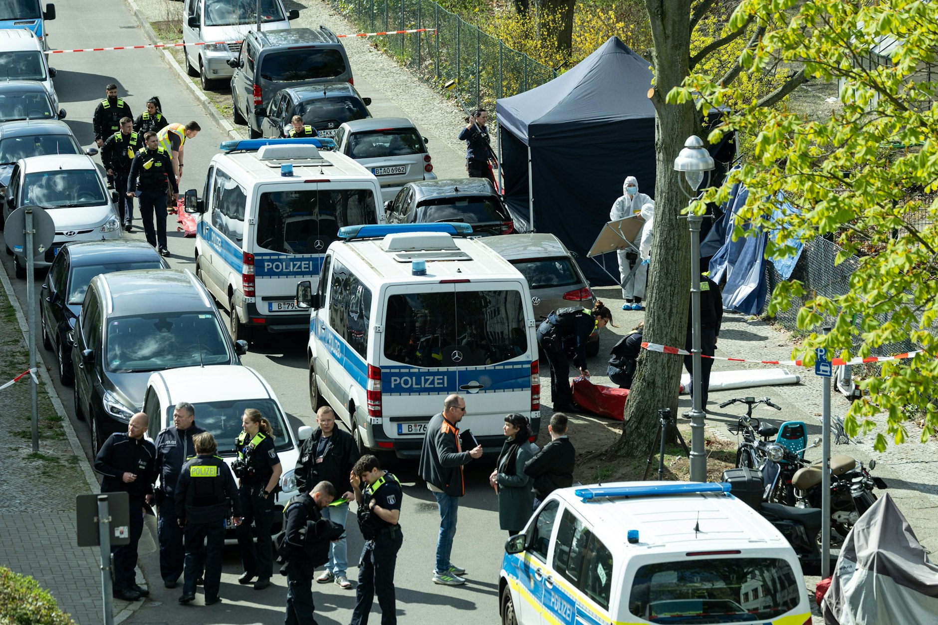Polizisten und Beamte der Spurensicherung in weißen Schutzanzügen stehen am Fundort. Wegen einer männlichen Leiche wurde die Polizei am Morgen des 9. April 2025 alarmiert.
