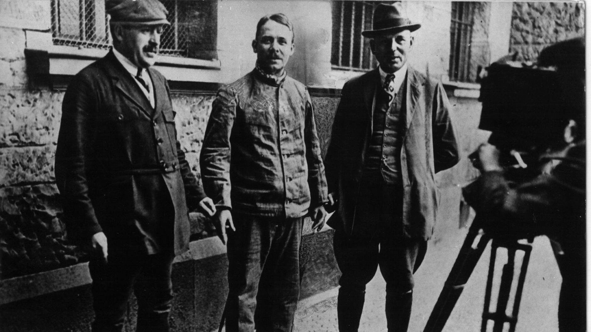 Fritz Haarmann (Mitte) wird von Kriminalbeamten in Handschellen gehalten und gefilmt.