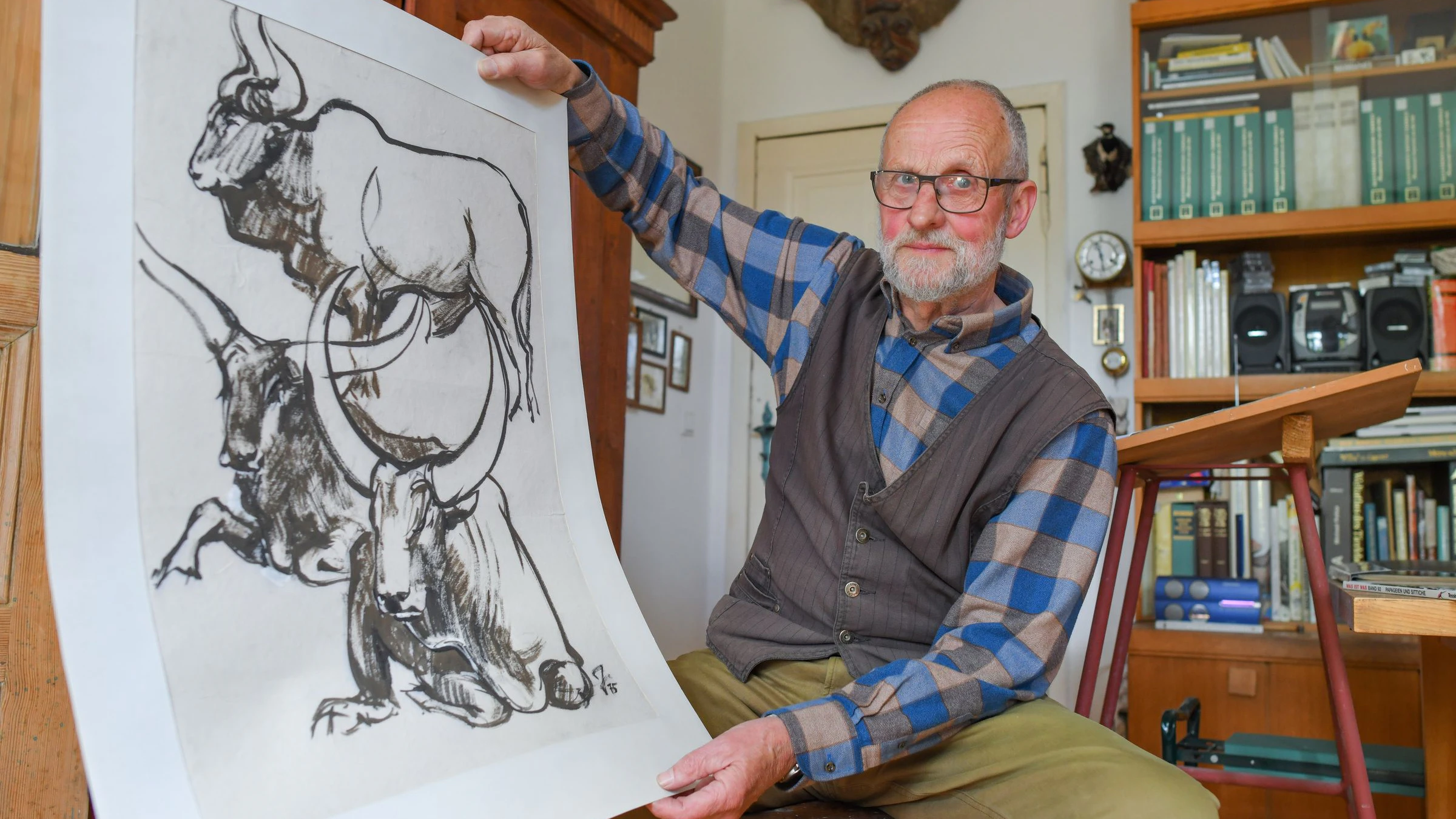 Reiner Zieger sitzt in seinem Atelier, zeigt eine Pinselzeichnung von Watussirindern.