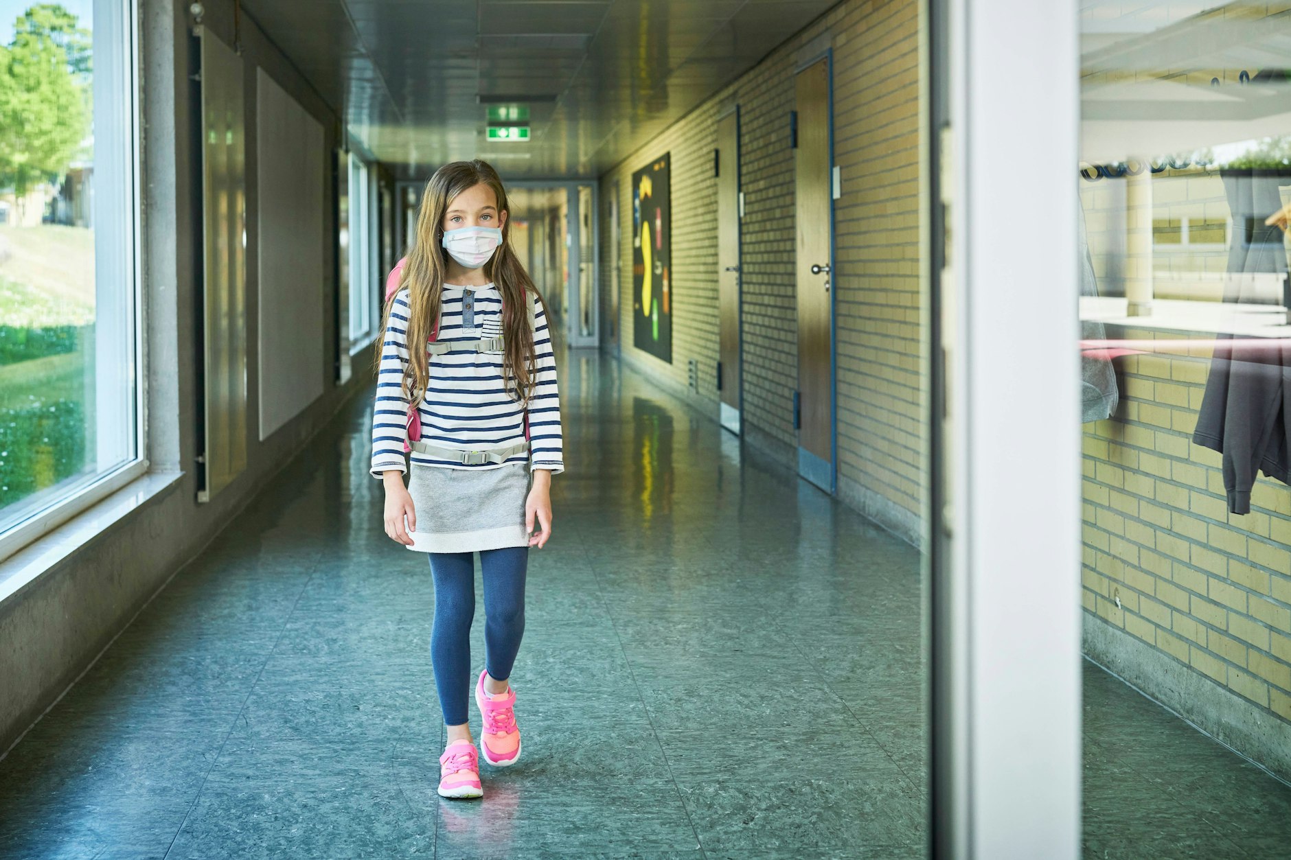 Symbolbild: Kind mit einer Maske auf einem Schulflur. Das Mädchen ist nicht Julia aus Berlin.