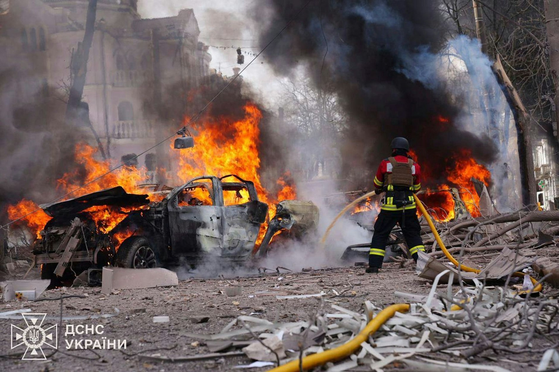 Ukraine, Sumy: Feuerwehrleute löschen nach dem russischen Raketenangriff auf das Zentrum der Stadt ein brennendes Auto.