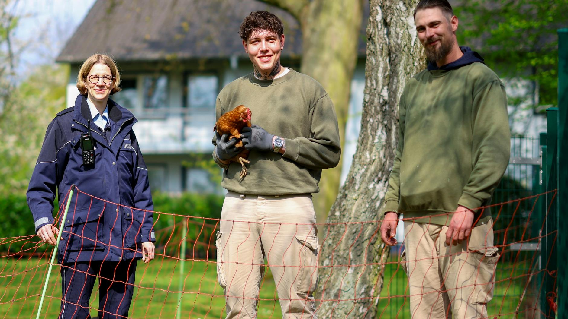 Die Vollzugsbeamtin Anika Schäfer ist für das Hühnerprojekt der JVA zuständig. Die Häftlinge Ryan (li.) und Manuel kümmern sich um das geschundene Federvieh.