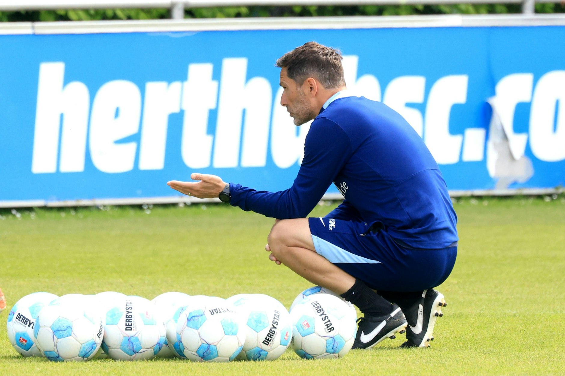 Trainer Stefan Leitl hockt vor vielen Bällen, im Hintergrund eine Bande mit der Aufschrift Hertha BSC.