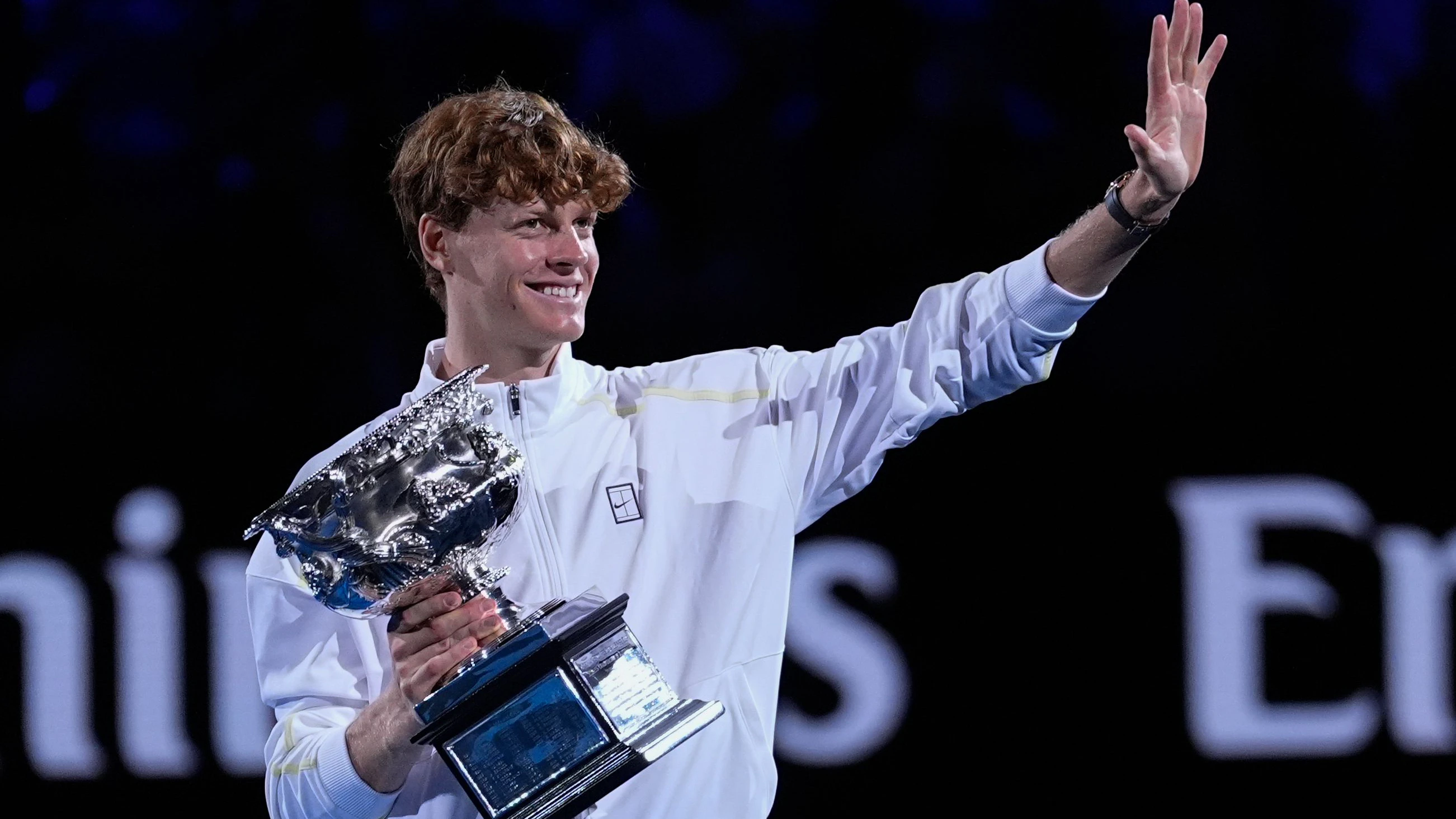 Jannik Sinner lächelt und winkt mit dem Norman Brookes Challenge Cup in der Hand nach seinem Sieg bei den Australian Open.