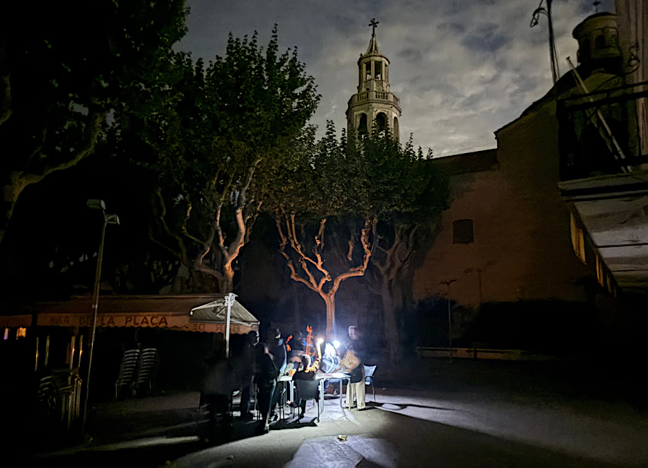 Auf der Plaza del Ajuntament sitzen die Gäste eines Straßencafés in der Kleinstadt Premià de Mar bei Barcelona an der Kirche San Cristòfol bei einem Stromausfall im Licht von Taschenlampen und trinken lauwarmes Bier.