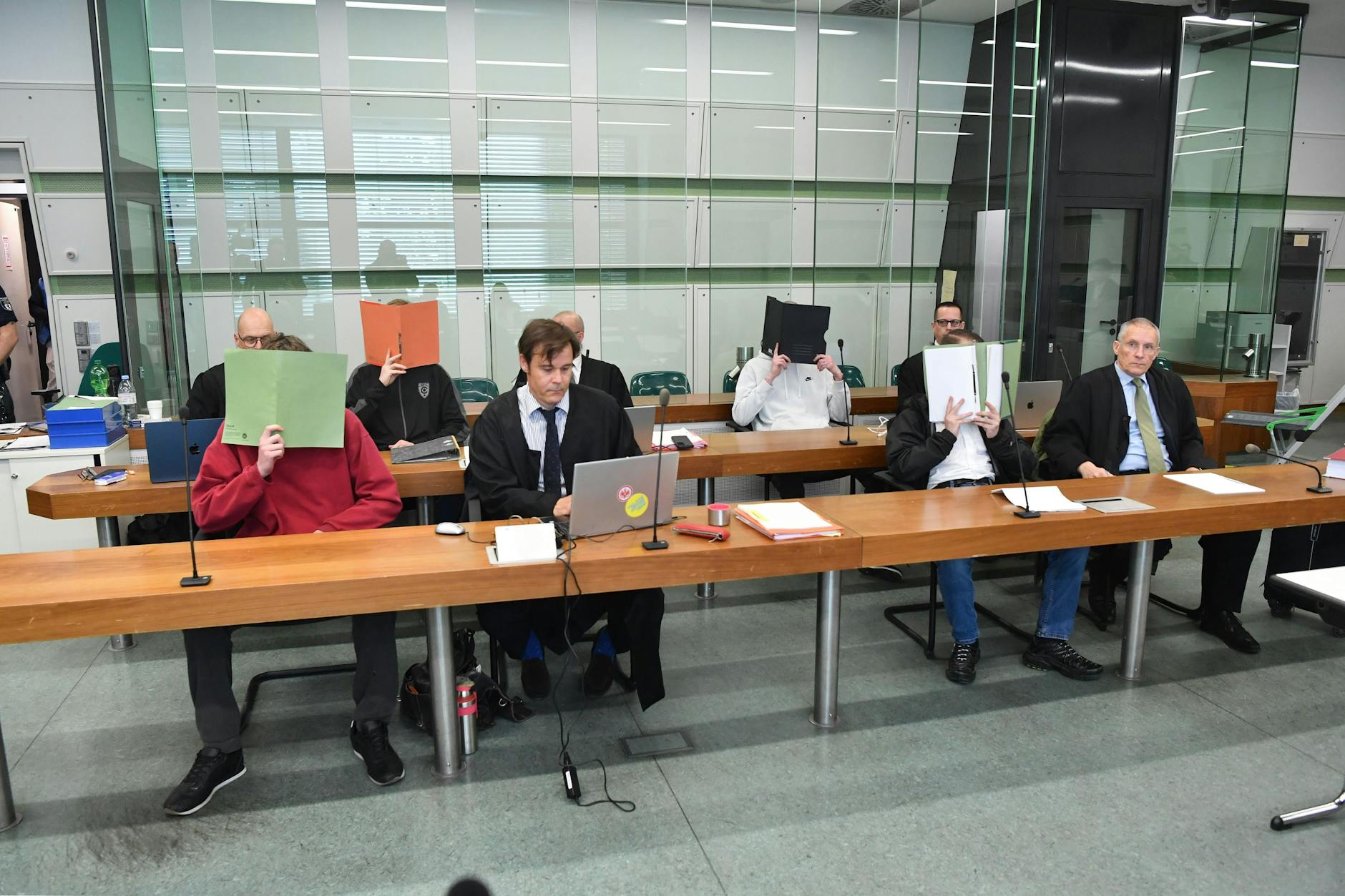 Prozessauftakt gegen die vier Neonazis, unschwer erkennbar an den Aktendeckeln vorm Gesicht.