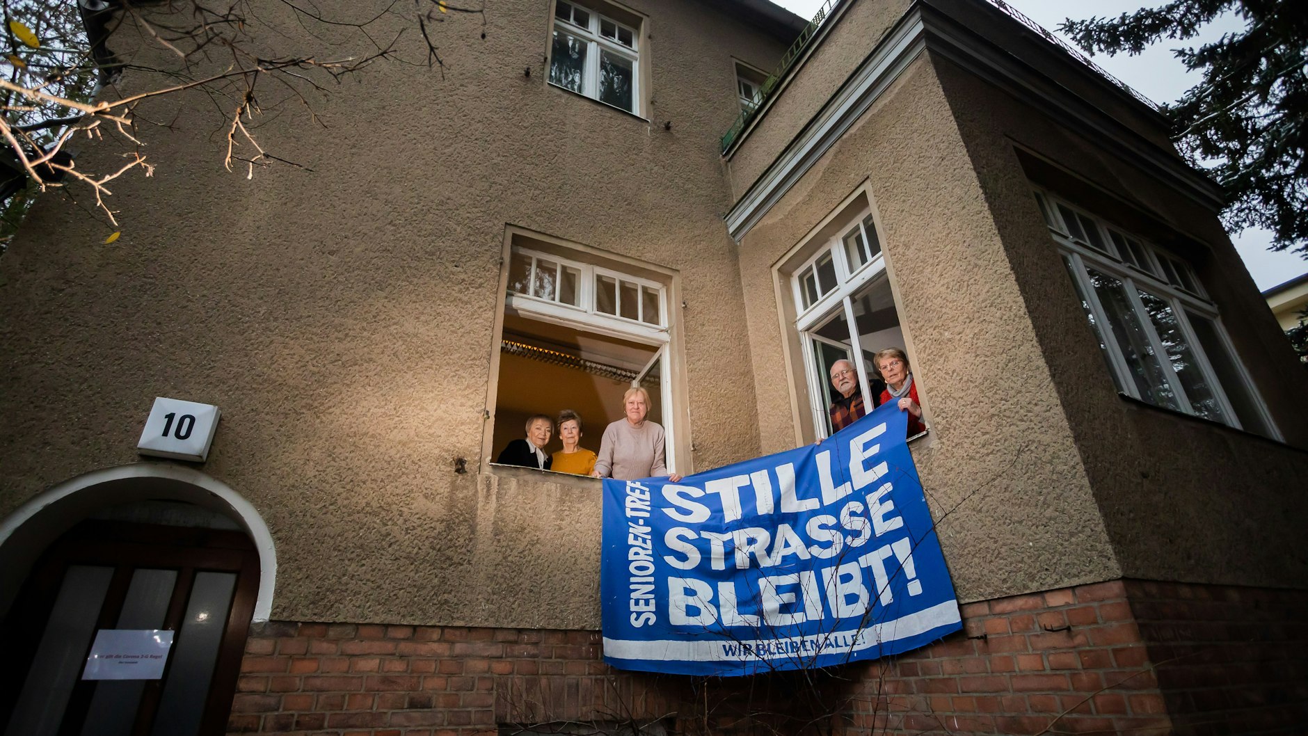 Elli Pomerenke (l-r), Ingrid Pilz, Margret Pollak, Peter Klotsche und Brigitte Klotsche, ehemalige Hausbesetzer, halten 2021 am Fenster der „Begegnungsstätte für Jung und Alt“ in der Stille Straße 10 in Berlin-Pankow ein altes Protestbanner.