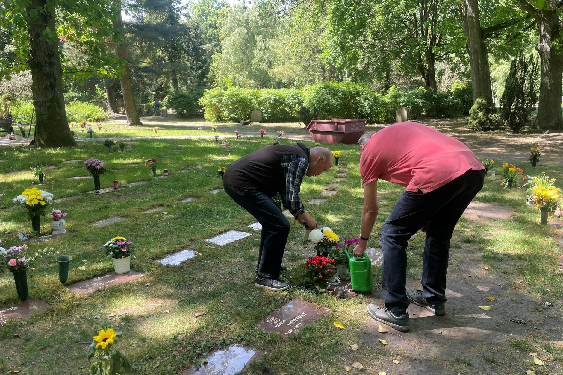 Zwei Friedhofsbesucher gießen mit mitgebrachtem Wasser ihre Grabstellen.