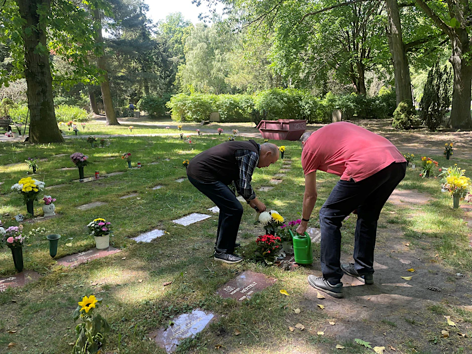 Zwei Friedhofsbesucher gießen mit mitgebrachtem Wasser ihre Grabstellen.