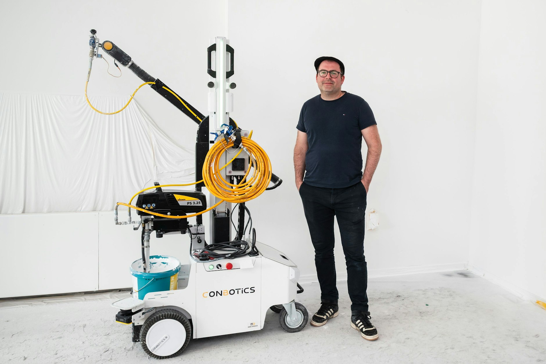 Philipp Heyne, Mitgründer des Berliner Start-ups ConBotics, neben dem Malerroboter im Labor des Unternehmens. Per Playstation-Steuerung streicht, spachtelt oder schleift der Roboter unermüdlich mit Vorliebe große Flächen.