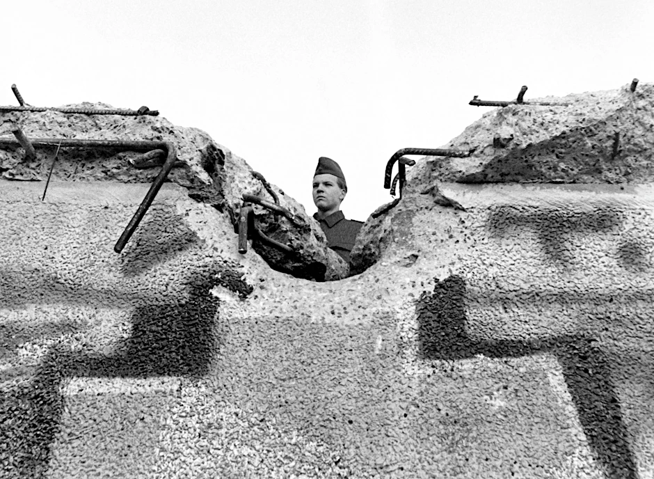 Ein Soldat der DDR-Grenztruppen schaut über eine zerstörte Mauer. Ein Foto vom 12.11.1989.