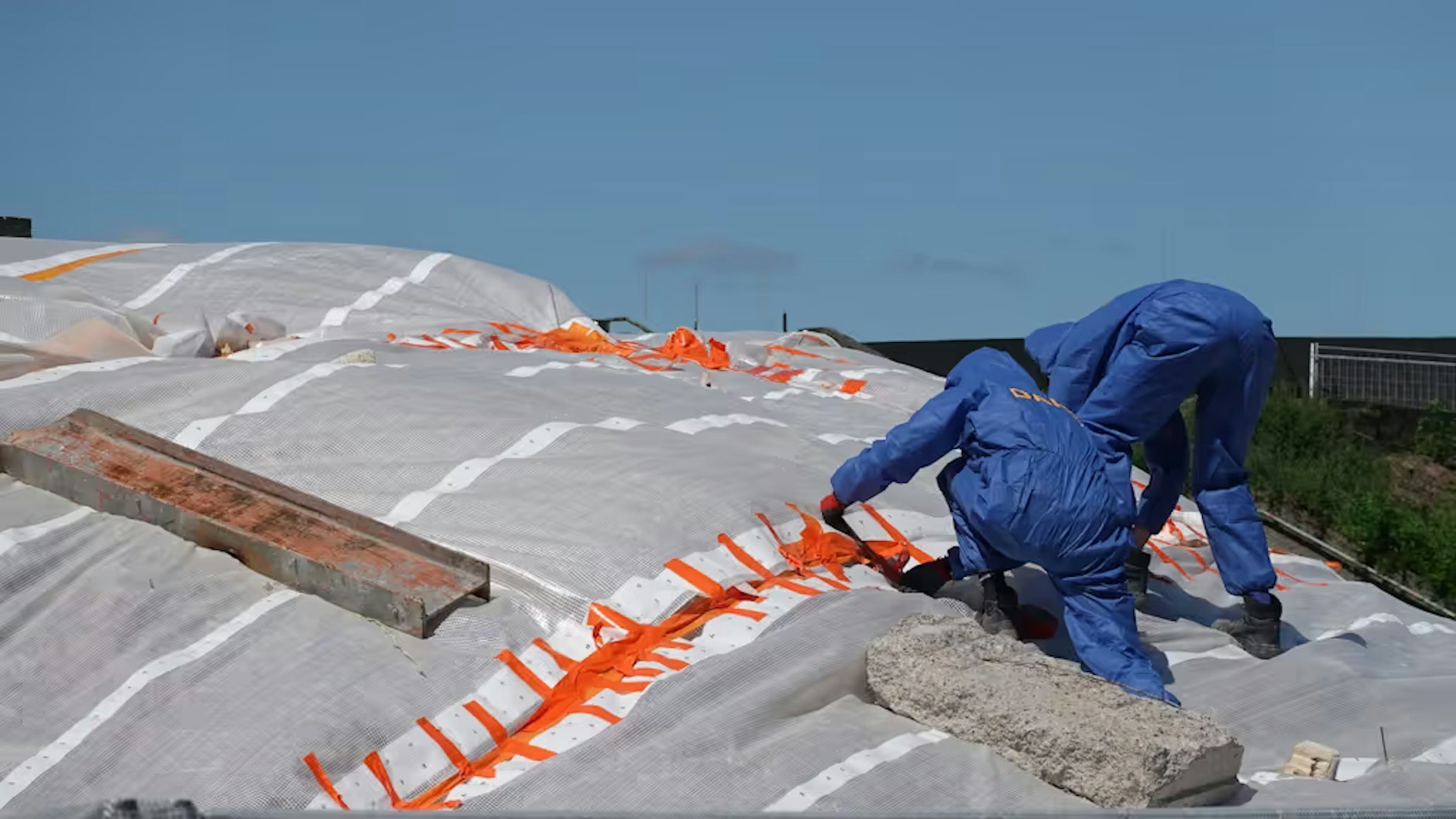 Bauarbeiter in Schutzanzügen spannen eine Folie über die Schuttberge und verkleben die Verbindungsstellen.