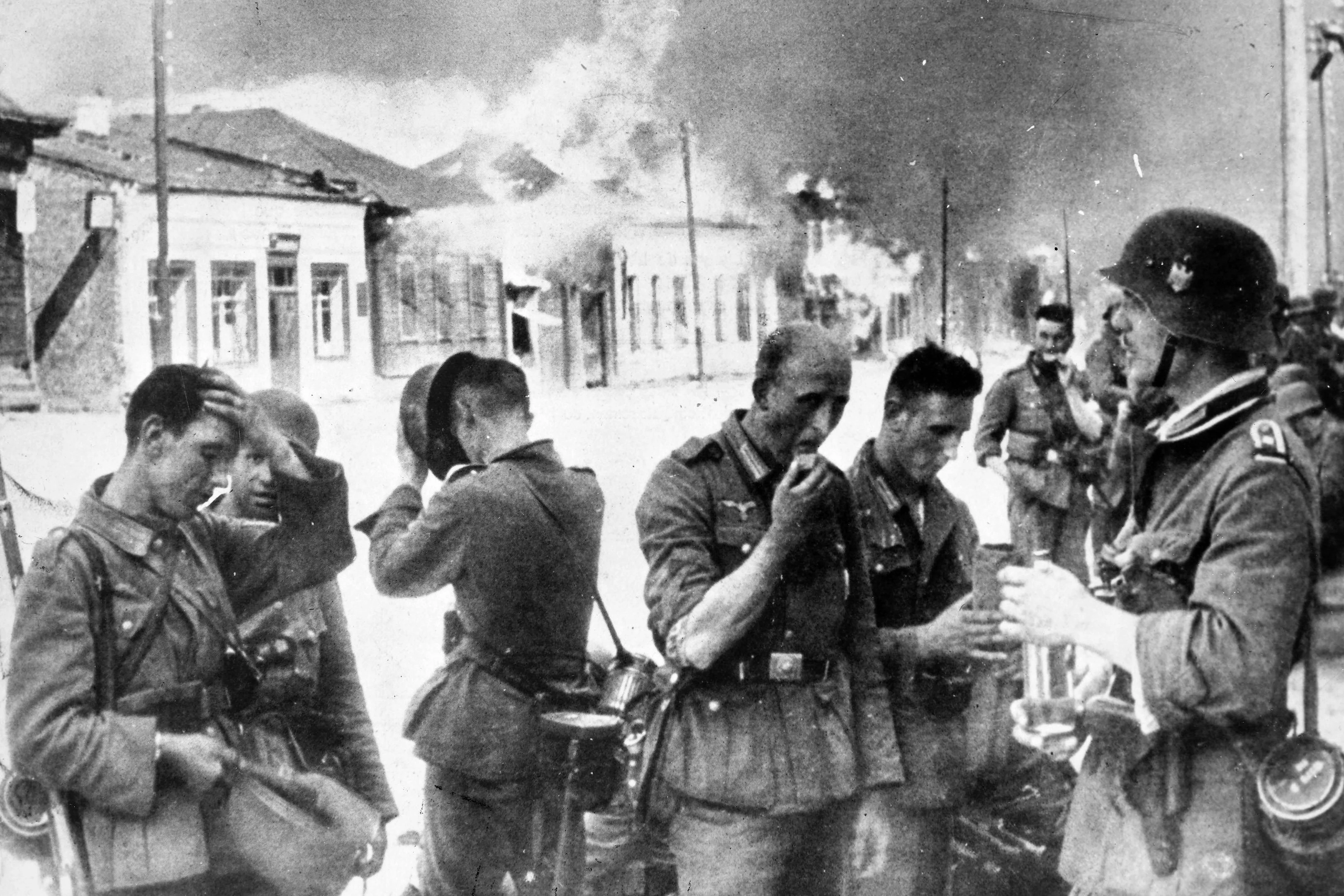 Soldaten der Wehrmacht pausieren vor den brennenden Häusern einer russischen Stadt, 1941.
