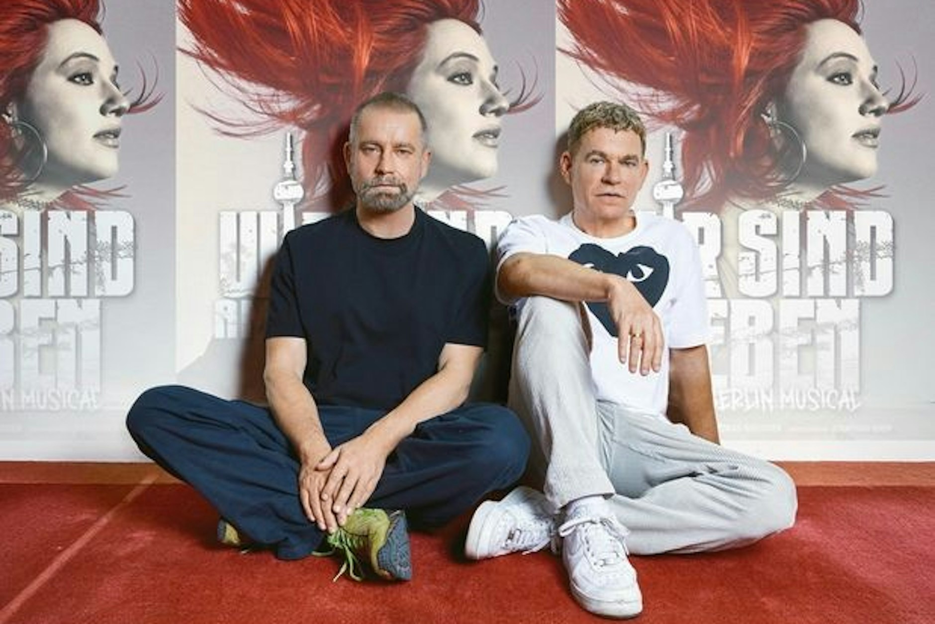 Rosenstolz-Musiker Peter Plate und Ulf Leo Sommer sitzen vor Plakaten ihres neuen Musical-Projekts Wir sind am Leben.
