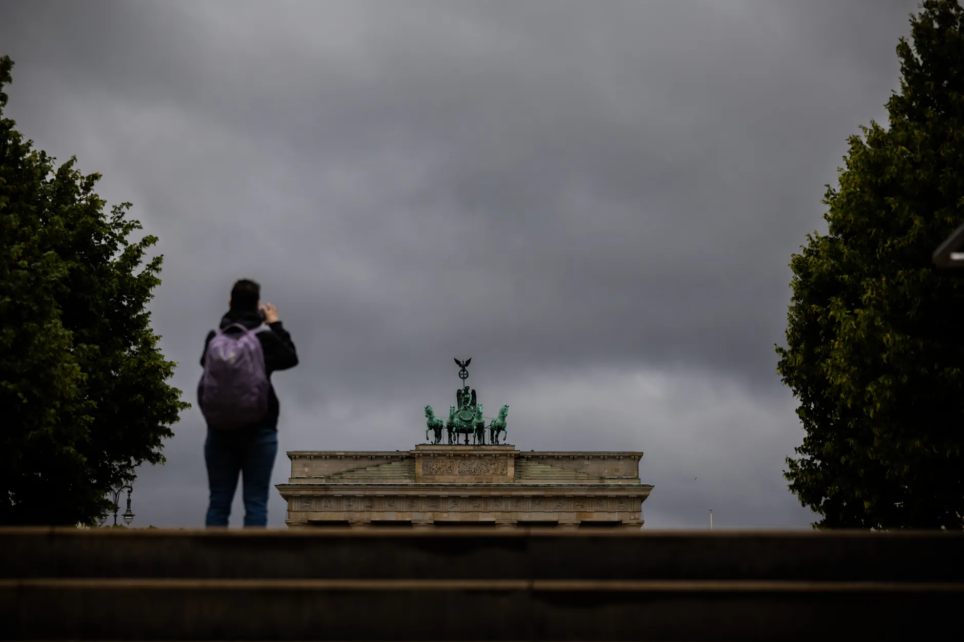 Eine Person fotografiert bei wolkenverhangenem Himmel das Brandenburger Tor.
