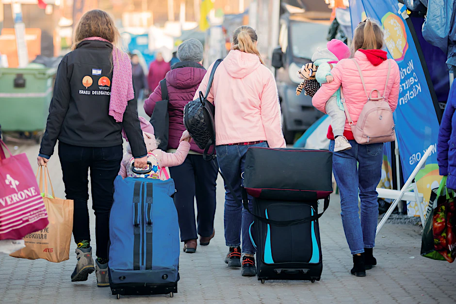 Frauen und Kinder, die aus der Ukraine geflohen sind, werden im Februar 2022 am Grenzübergang Medyka, kurz hinter der ukrainischen Grenze, auf polnischer Seite, von einer freiwilligen Helferin (l) begleitet.