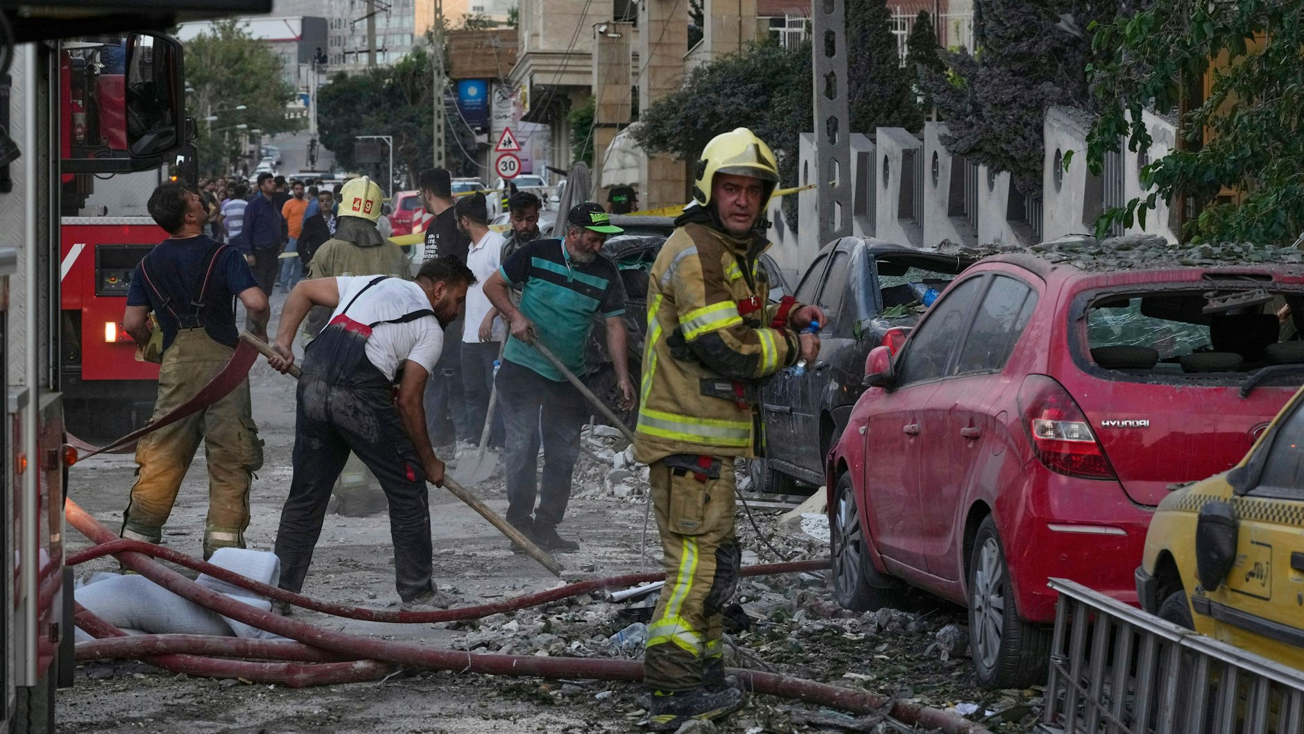 Feuerwehrleute und Menschen säubern den Schauplatz einer Explosion in einer Wohnanlage nach einem israelischen Angriff auf die iranische Hauptstadt Teheran. 