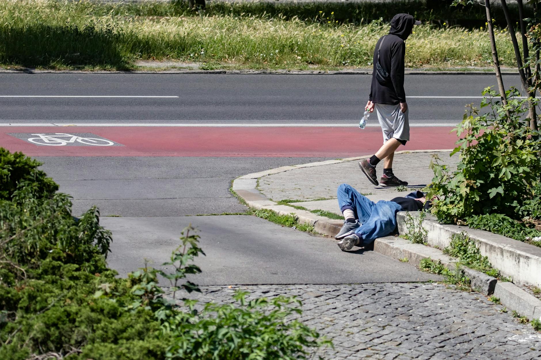 Ein obdachloser Mann liegt am Ostbahnhof auf dem Gehsteig, ein anderer geht achtlos vorbei.