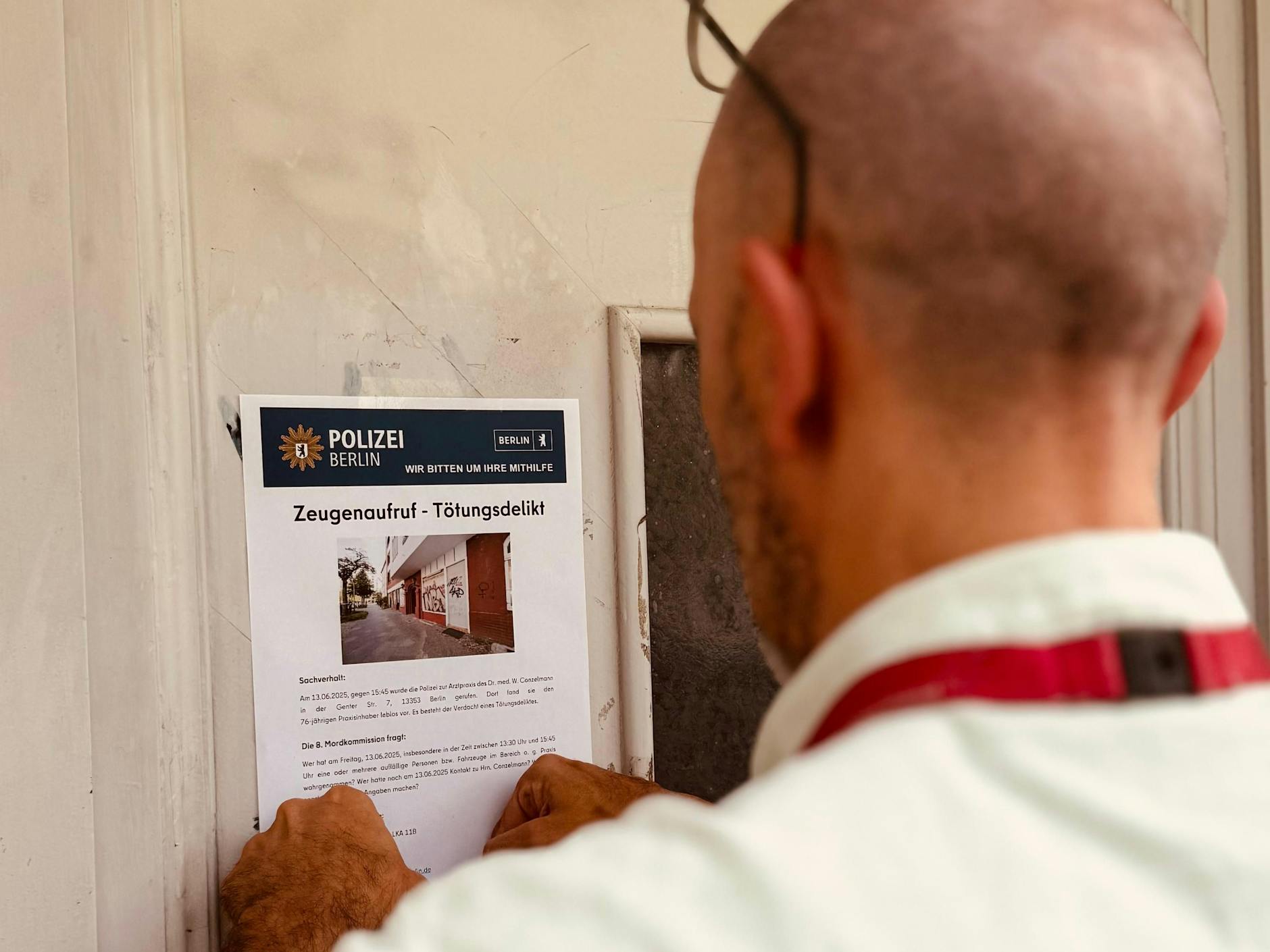 Ein Ermittler klebt in der Genter Straße ein Plakat mit dem Zeugenaufruf im Fall des getöteten Arztes Wolfgang Conzelmann.