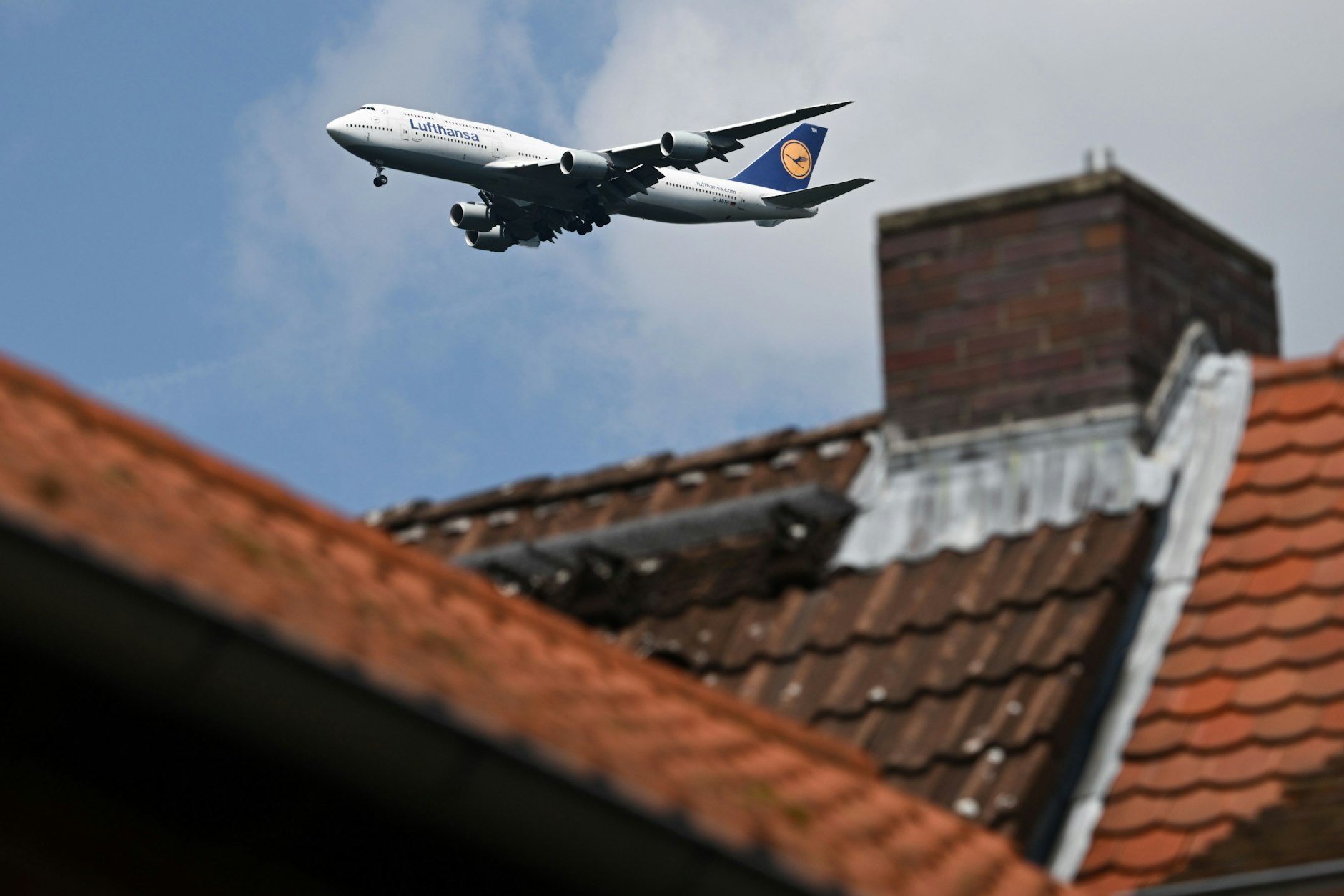 Eine Boeing 747-830 der Lufthansa ist hinter einem Haus im Landeanflug auf den Frankfurter Flughafen.