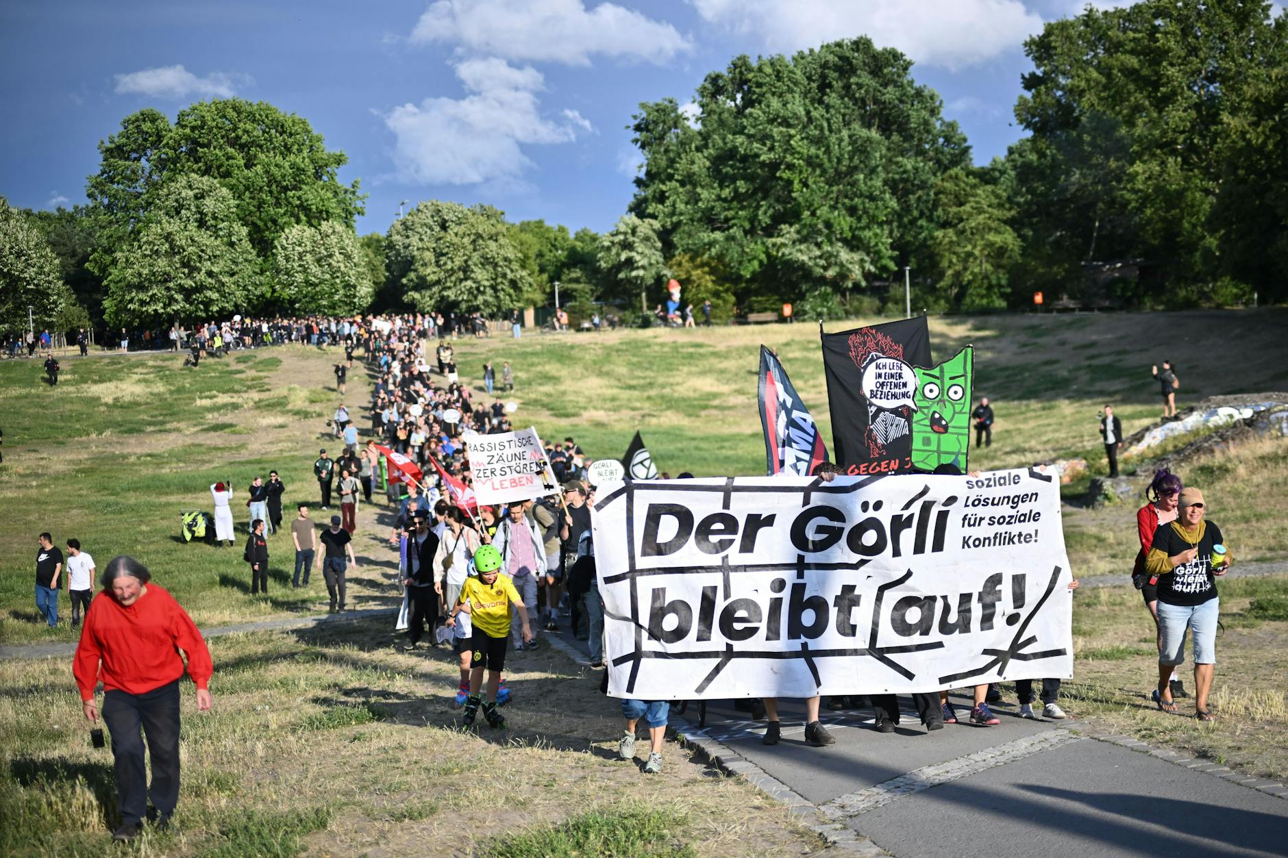 Berlin: Demonstrierende gehen hinter einem Banner mit der Aufschrift „Der Görli bleibt auf!“ bei einer Demonstration gegen den geplanten Zaunbau um den Görlitzer Park durch den Park.
