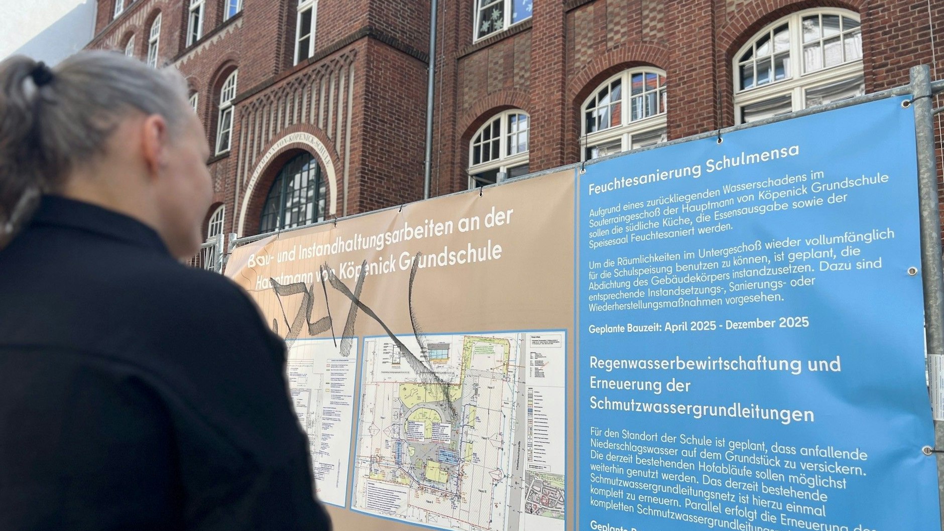 Bezirkselternsprecherin Mone G. vor dem Bauschild an der Hauptmann-von-Köpenick-Grundschule: Bis Ende des Jahres soll die Mensa saniert werden.