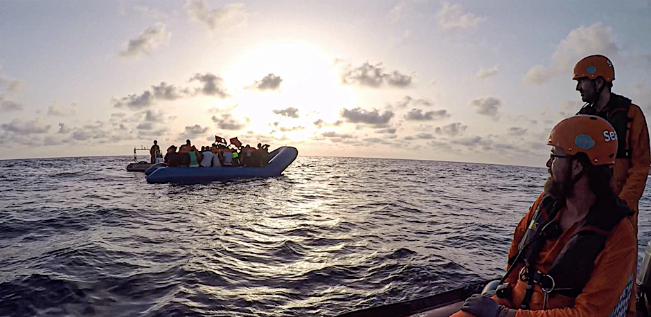 Die von der Seenotrettungsorganisation Sea-Eye herausgegebene Aufnahme zeigt Seenotretter vom Rettungsschiff „Alan Kurdi“, die zu einem Schlauchboot voller Flüchtlinge schauen.