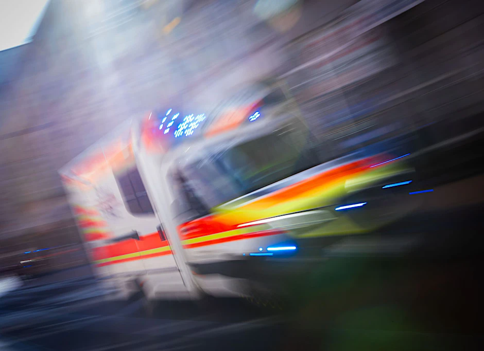 Ein Rettungsfahrzeug ist mit Blaulicht auf einer Straße in der Innenstadt unterwegs.