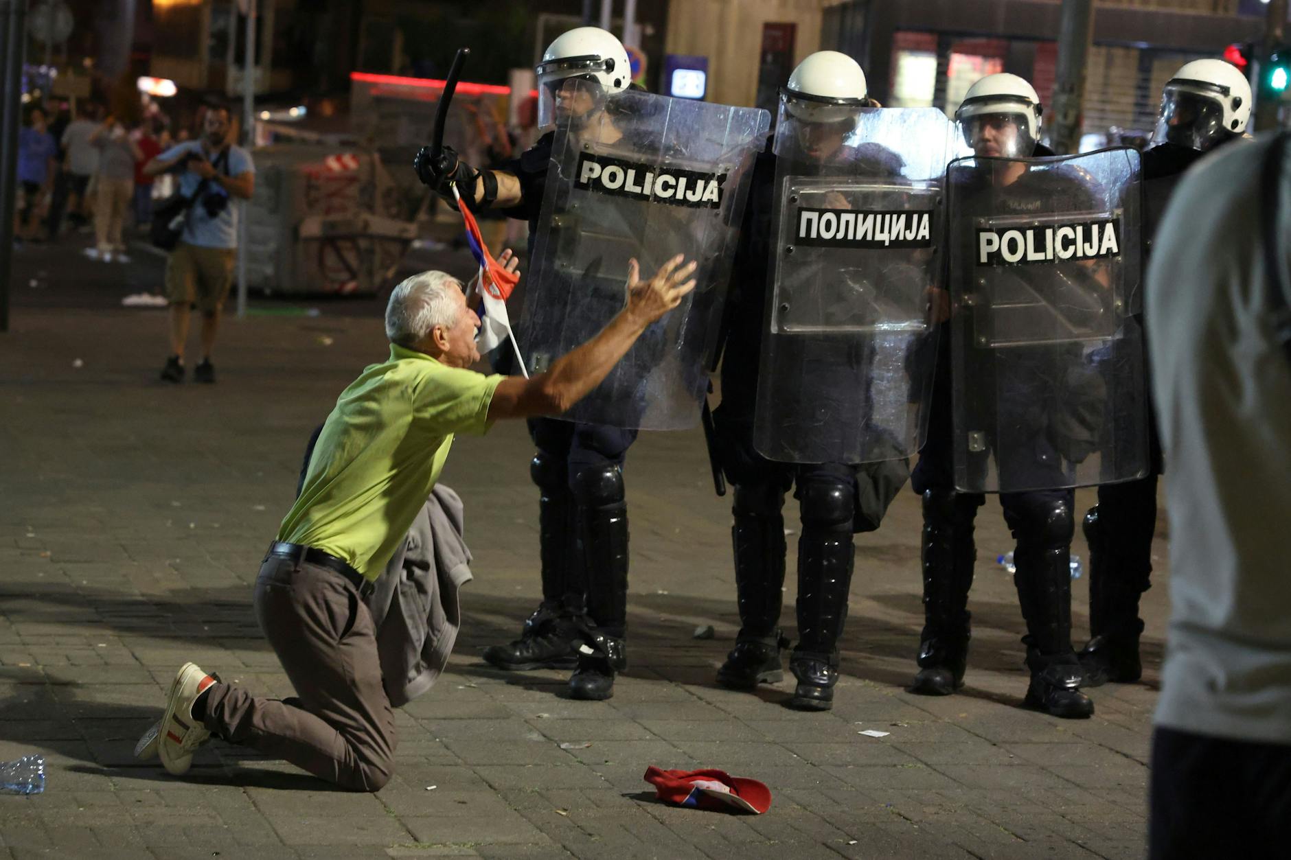 28.06.2025, Serbien, Belgrad: Ein älterer Mann kniet vor einer Polizeikette am Ende einer Kundgebung, bei der eine vorgezogene Wahl gefordert wurde.