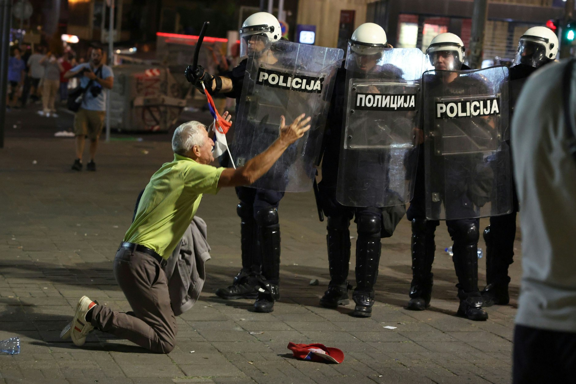 28.06.2025, Serbien, Belgrad: Ein älterer Mann kniet vor einer Polizeikette am Ende einer Kundgebung, bei der eine vorgezogene Wahl gefordert wurde.