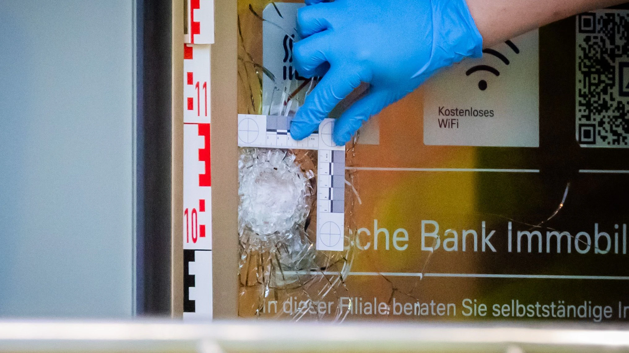 Ein Polizist vermisst und fotografiert eine Schussmarke an einer Bankfiliale am Kurfürstendamm.