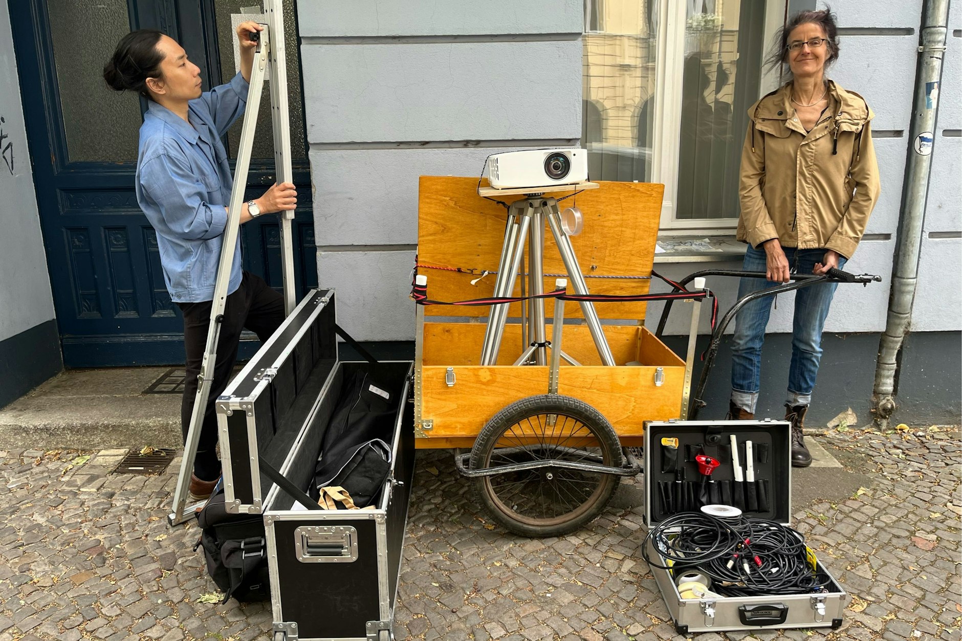 Auf dem Wagen der Beamer, links im Kasten die zusammengefaltete Leinwand, im Koffer unten rechts Kabel sowie das rote Glöckchen, mit dem zu Filmbeginn geläutet wird. So kommt das Moabiter Wander-Kino mit Maren Dorner und Jae-Pyung Park vom Verein Moabiter Filmkultur e. V. überall hin.