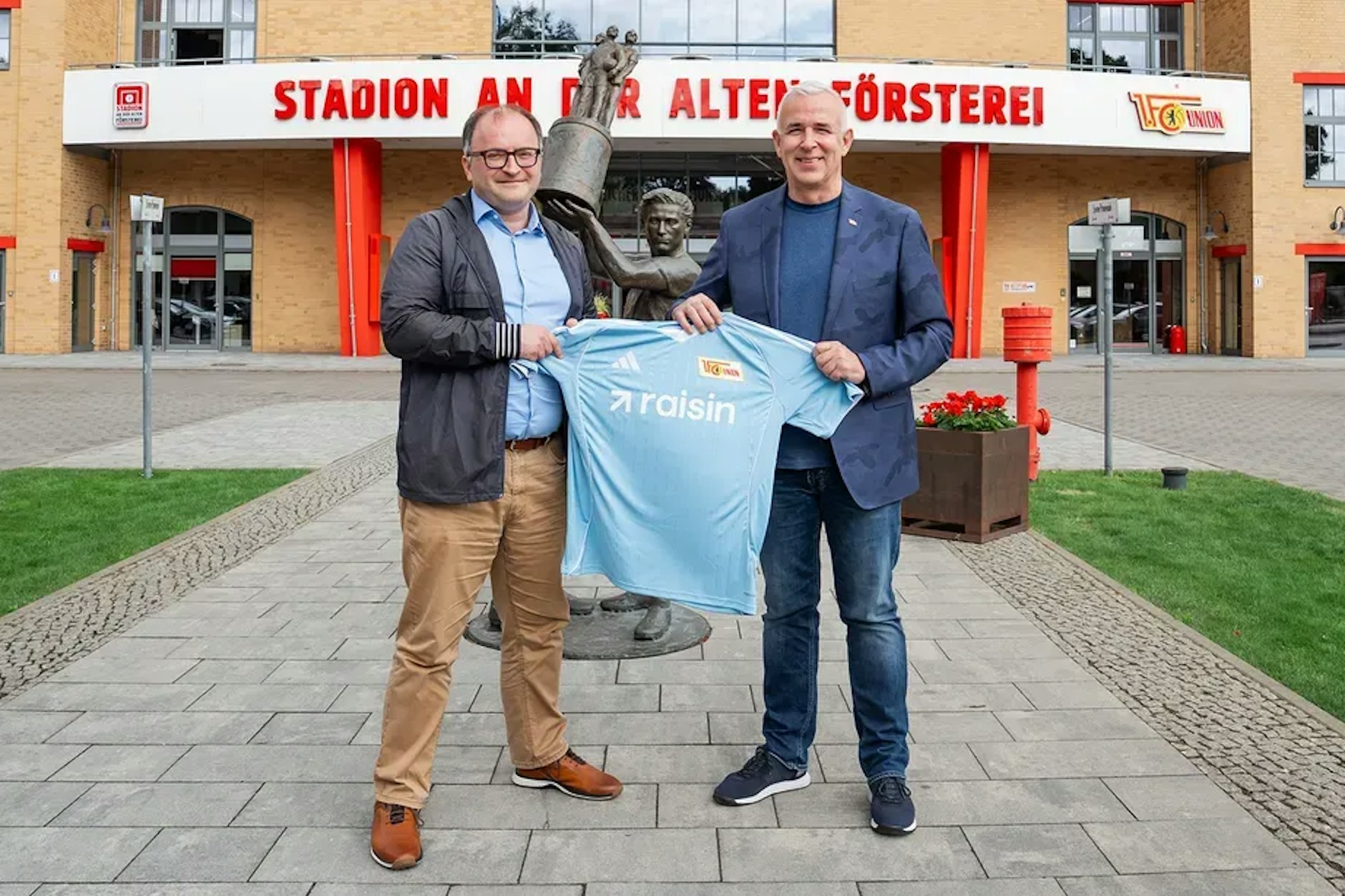 Union-Präsident Dirk Zingler (rechts) und Raisin-CEO Tamaz Georgadze präsentieren vor der Alten Försterei das neue himmelblaue Auswärtstrikot mit dem Raisin-Aufdruck.