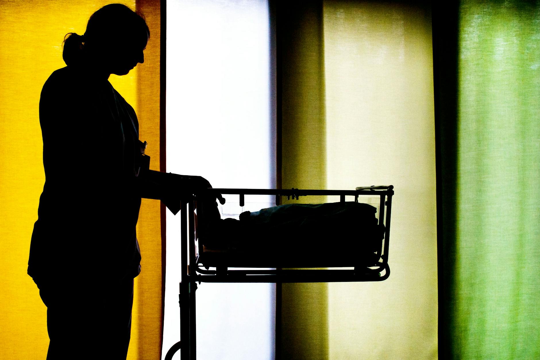 Eine Hebamme steht neben einem Säuglingsbett in einer Klinik für Frauenheilkunde und Geburtshilfe.