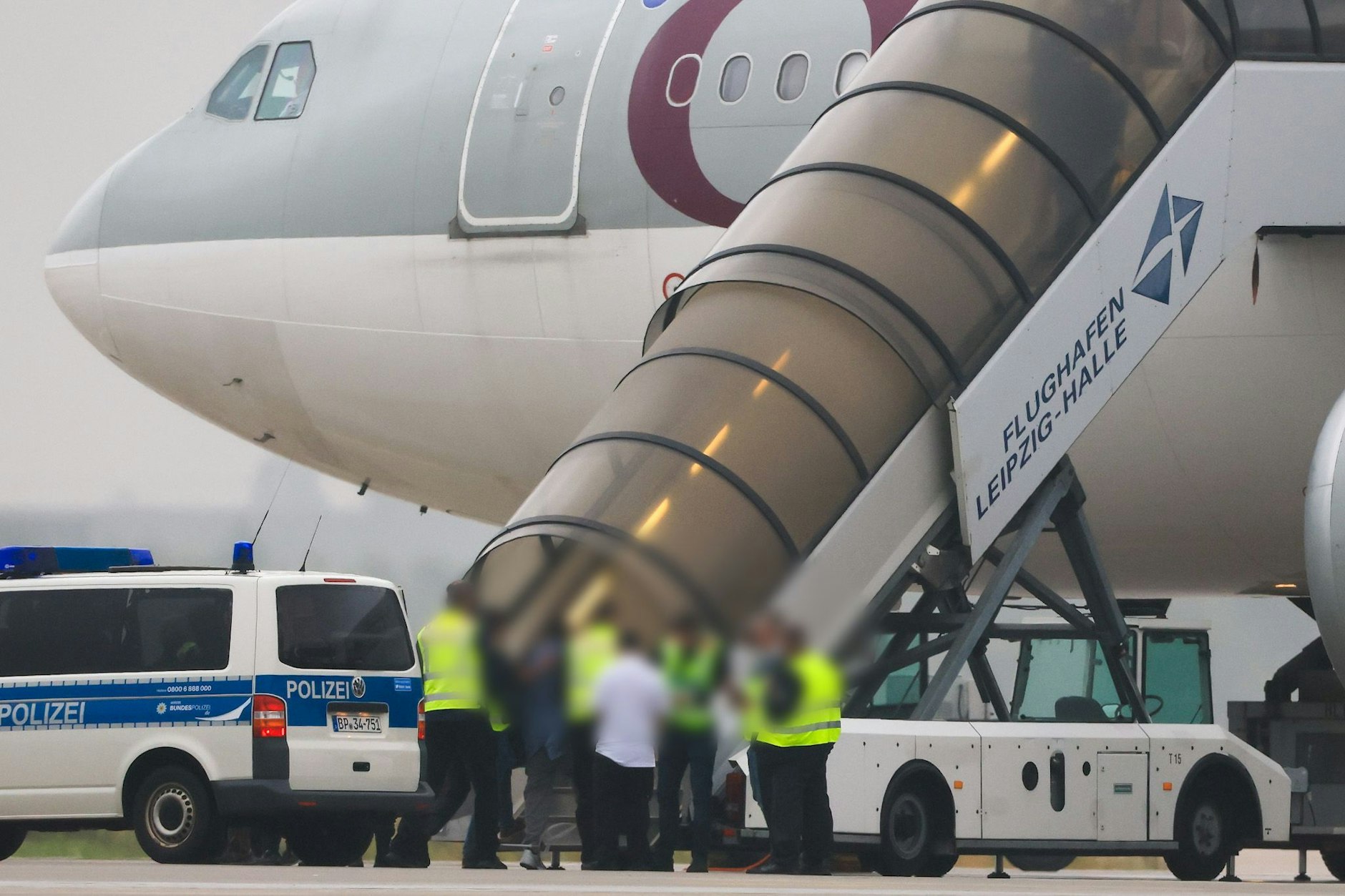 Menschen besteigen ein Flugzeug der Qatar Airways, vor dem Fahrzeuge der Bundespolizei auf dem Vorfeld am Flughafen Leipzig/Halle stehen.