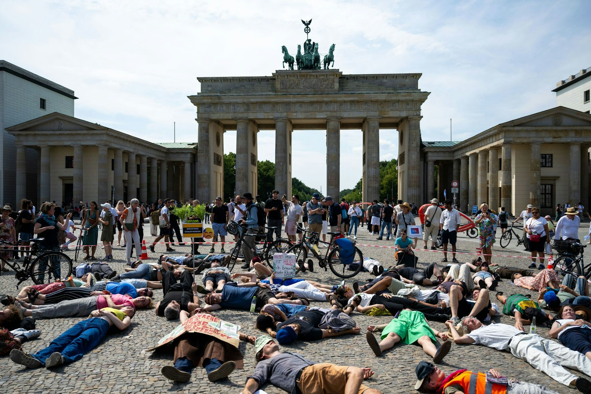 Irres Bild: Etliche Menschen legten sich am Sonntag vor dem Brandenburger Tor auf die Straße. Sie setzen sich dafür ein, dass die Stadt Berlin besser gegen Hitze geschützt wird.