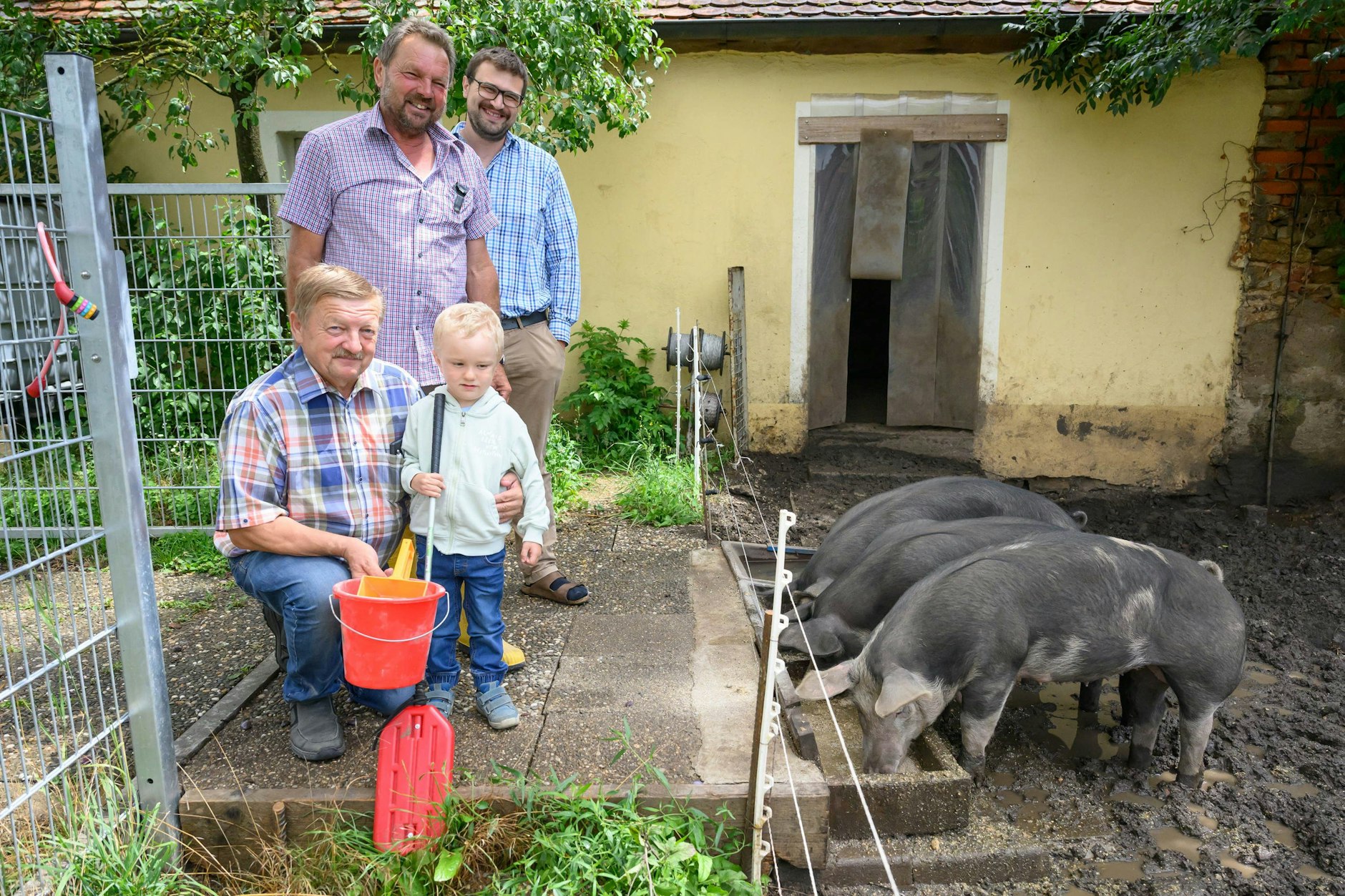 Karl und Gerhard Weinländer mit Enkel Noah und Pfarrer Christian Dellert füttern die Duroc-Schweine Lina, Frederick und Tinkia.
