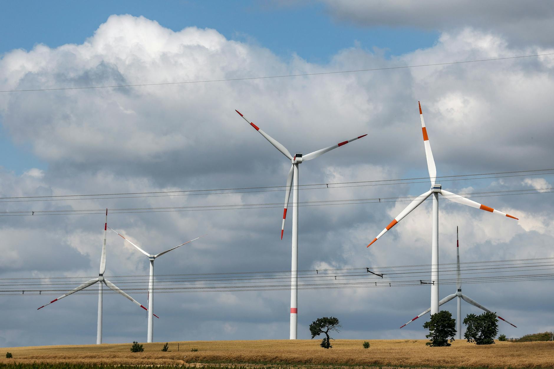 Windräder drehen sich hinter einer Hochspannungsleitung auf einem Feld bei Riesa unter grauen Wolken am 17. Juli 2025 in Riesa, Sachsen.