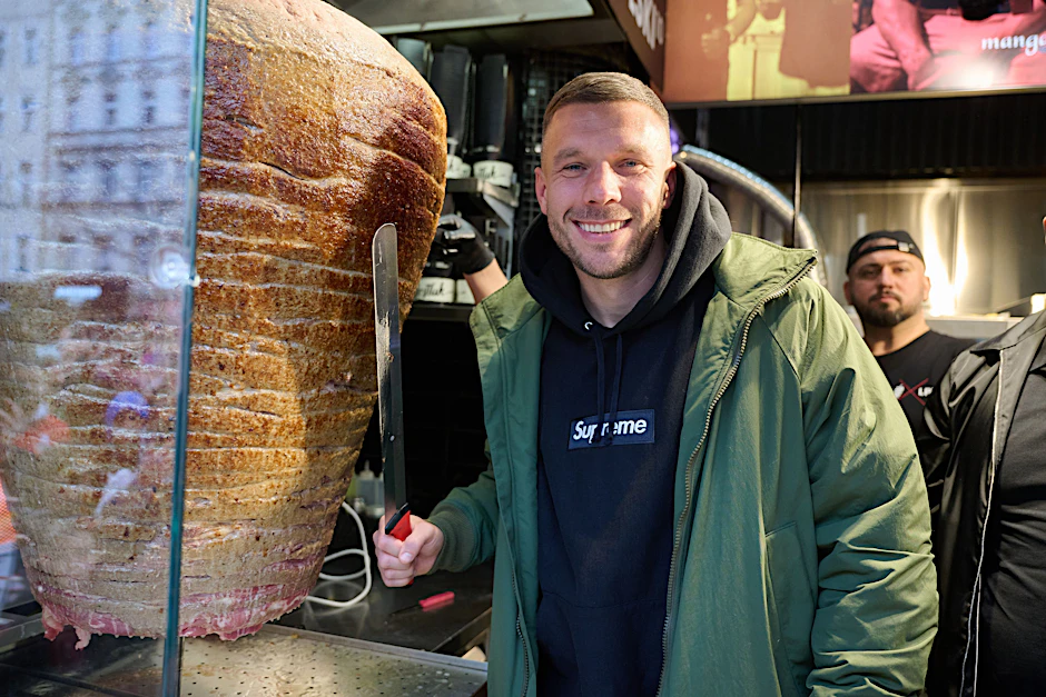 Lukas Podolski, ehemaliger Fußballprofi und Unternehmer, steht an einem Drehspieß während der Eröffnung von Podolskis Döner-Imbiss in Berlin.