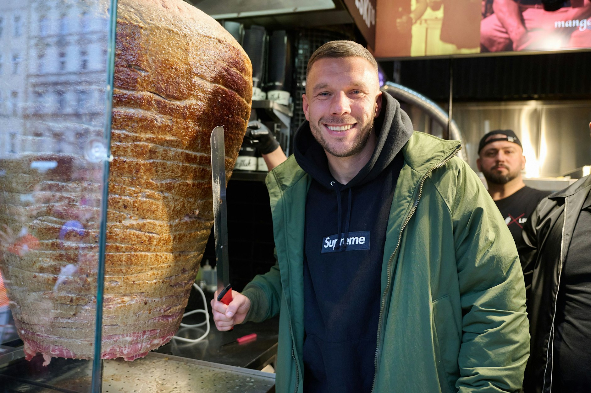 Lukas Podolski, ehemaliger Fußballprofi und Unternehmer, steht an einem Drehspieß während der Eröffnung von Podolskis Döner-Imbiss in Berlin.