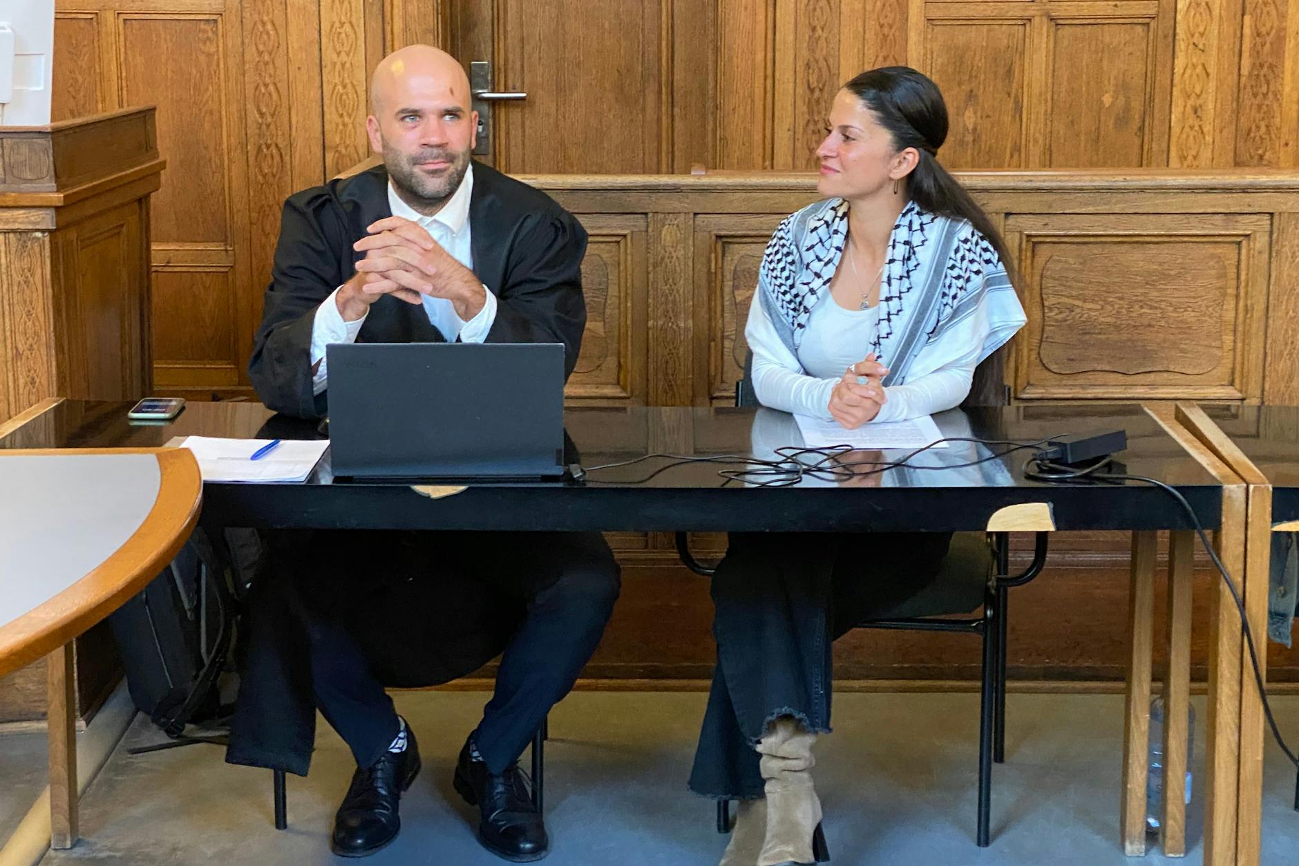 Die propalästinensische Aktivistin Yasemin Acar sitzt mit einem Palästinensertuch neben ihrem Anwalt Matthias Schuster.