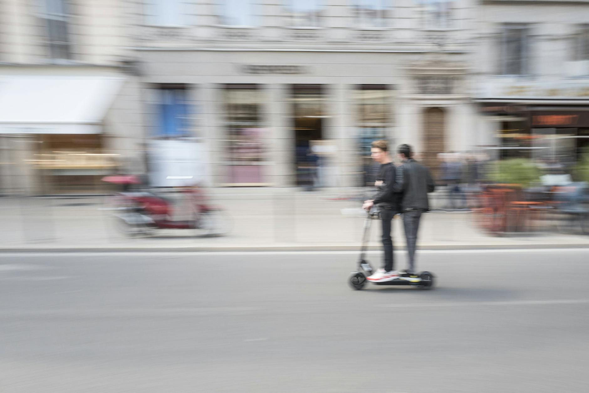 Zwei Männer auf einem E-Scooter fahren auf der Straße.