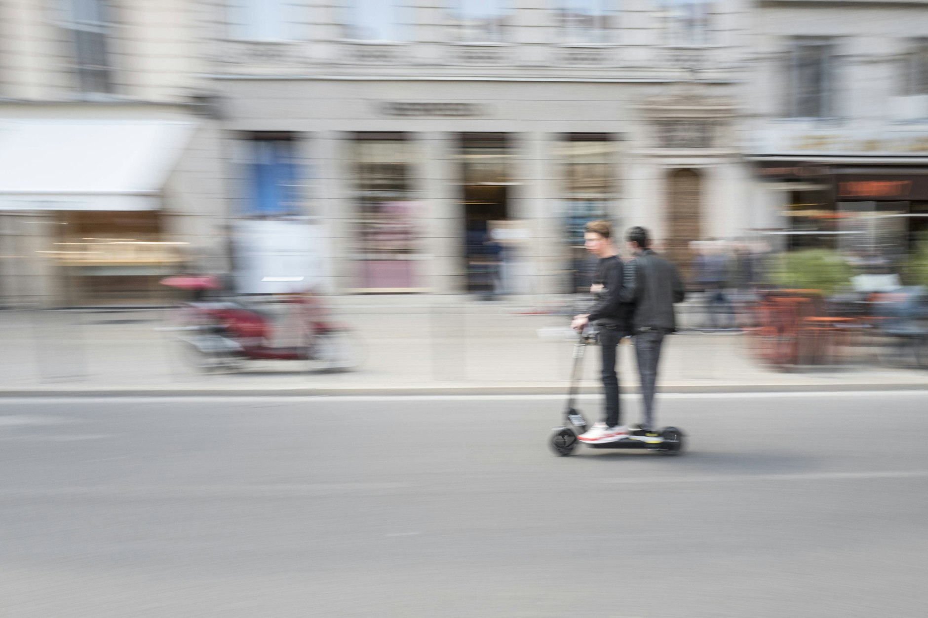 Zwei Männer auf einem E-Scooter fahren auf der Straße. 