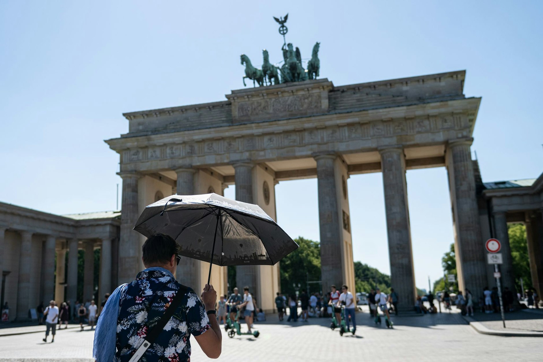 Eine Person läuft mit Schirm bei hohen Temperaturen über den Pariser Platz vor dem Brandenburger Tor.