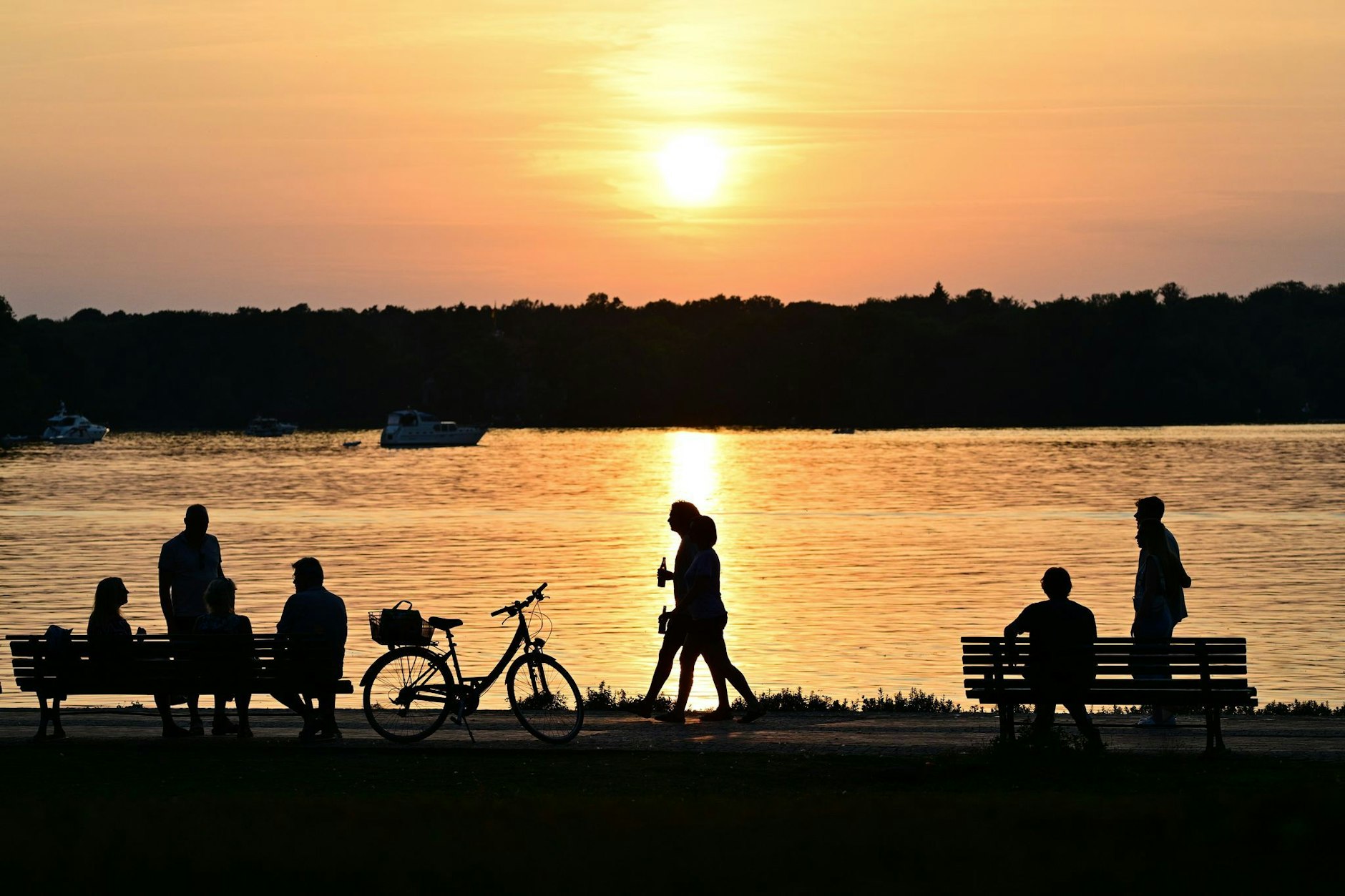 Menschen gehen bei Sonnenuntergang am Ufer des Tegeler Sees. (zu dpa: «Bilder des Tages»)