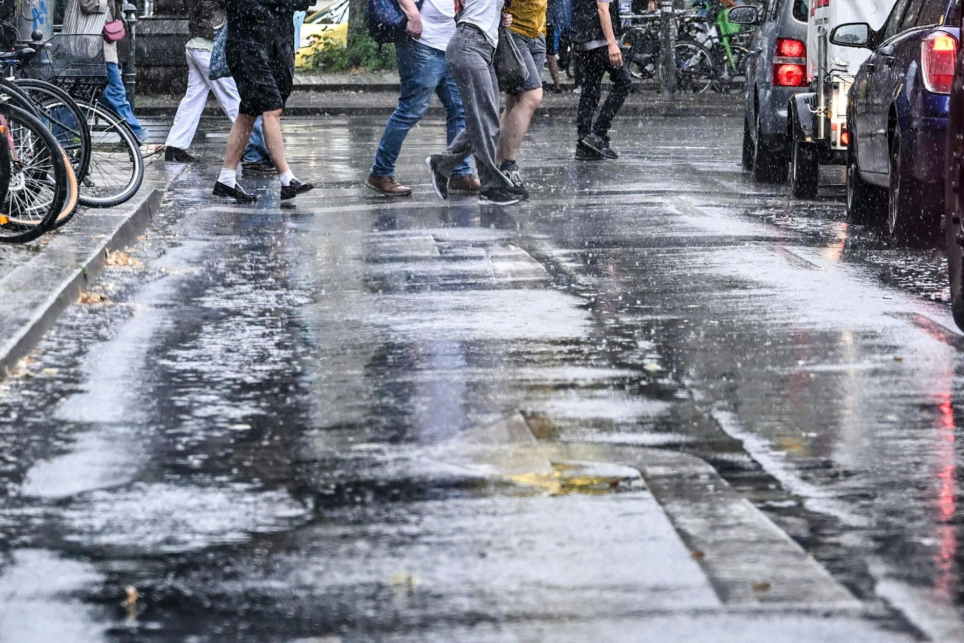 Passanten gehen bei einem heftigen Regenguss am U-Bahnhof Schlesisches Tor über die Straße. Sonne und Wolken wechseln sich in den nächsten Tagen in Berlin ab.