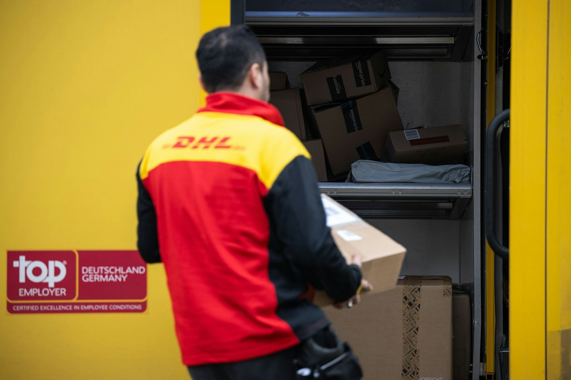 Ein DHL-Mitarbeiter trägt ein Paket in einen Lieferwagen.