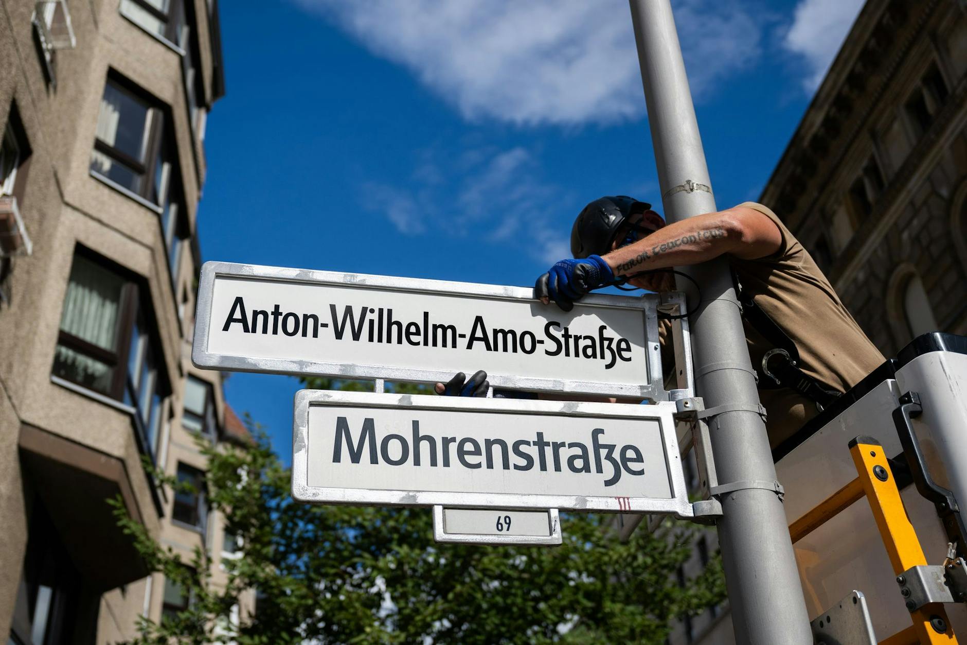 Ein Mitarbeiter einer Verkehrstechnikfirma hängt ein Straßenschild mit der Aufschrift Anton-Wilhelm-Amo-Straße über ein Schild mit der Aufschrift Mohrenstraße.