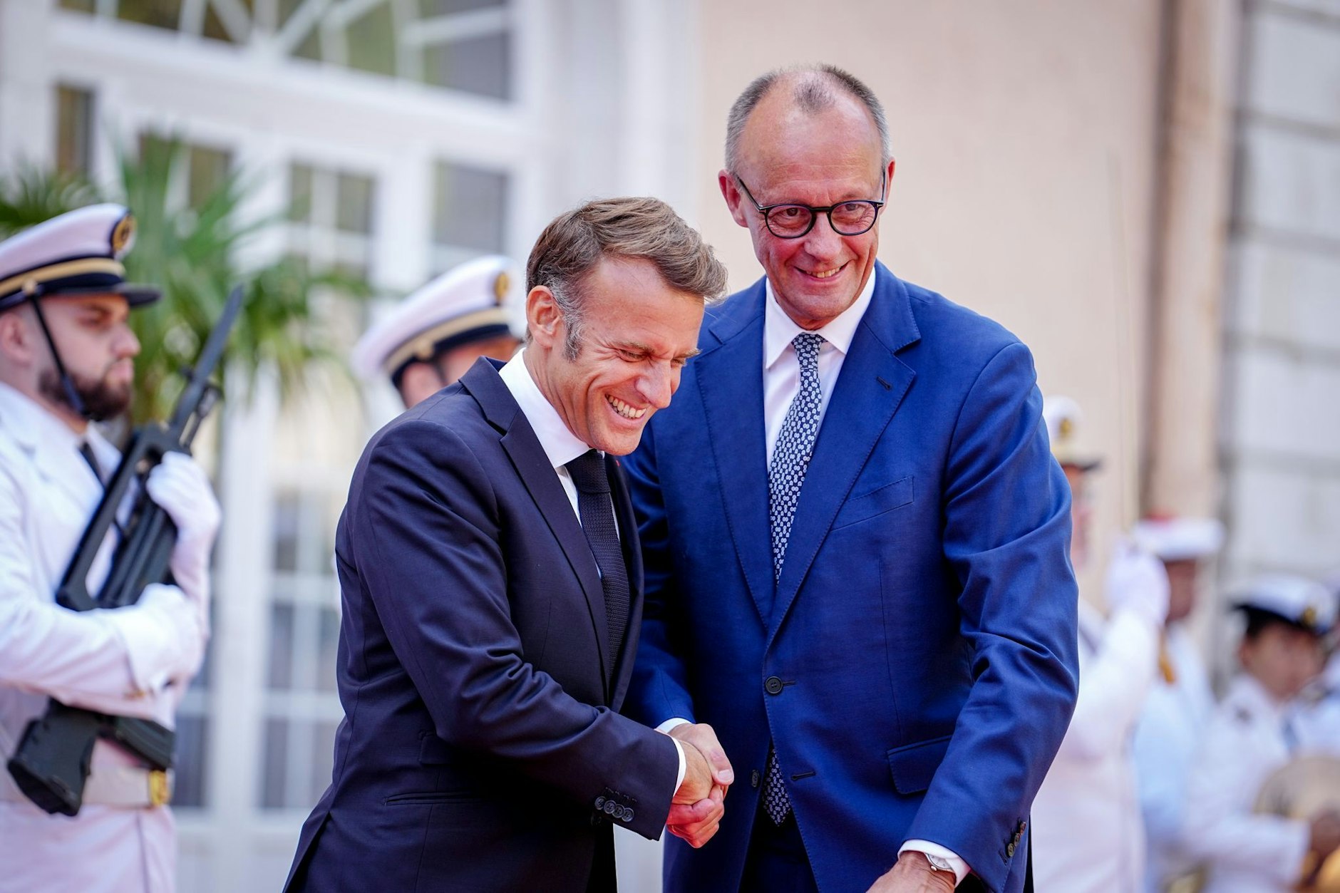 Bundeskanzler Friedrich Merz (r,CDU) und Frankreichs Präsident Emmanuel Macron begrüßen sich beim deutsch-französischen Regierungstreffen zur Wirtschafts- und Sicherheitspolitik.